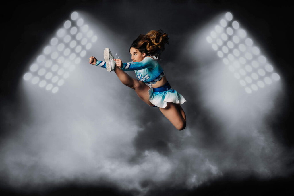 Competitive cheer sports portrait showing a cheerleader jumping in front of smoky stadium lights by Melissa Byrne Portrait Photographer based in Arizona.