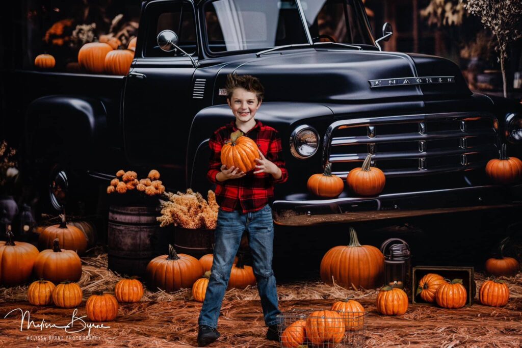 Young boy posing with pumpkins in front of a vintage truck.